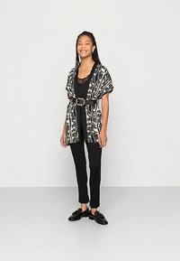 Juodas ir baltas raštuotas kimono su plačiomis rankovėmis, diržu juosmens srityje, derinamas su juodu viršutiniu drabužiu ir aptemptomis kelnėmis, dėvimas su juodais slip-on batais.