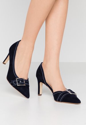 Granatowe zamszowe czółenka na 8 cm obcasie, z zaostrzonym noskiem, białym przeszyciem i ozdobną klamrą na cholewce.