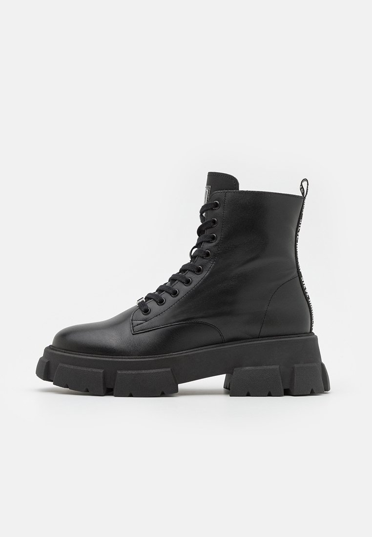 Botte de combat en cuir noir avec semelle épaisse et robuste, avant à lacets et languette à l'arrière, présentée de profil sur fond blanc.