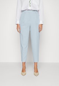 Light blue, tailored trousers with a slim fit, featuring a smooth texture and a clean waistband. Paired with beige pointed-toe shoes.