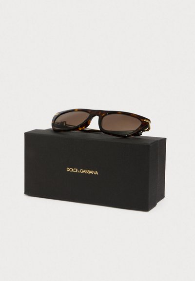 Kilpkonnakujulised prillid, millel on ristkülikukujulised raamid, tumeda pruuni objektiiviga ja kuldne detail, puhates mustal DOLCE & GABBANA karbil.