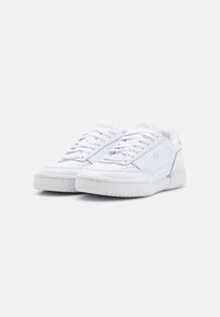 Witte leren sneakers met een platte zool, ronde neus en vetersluiting. Voorzien van perforaties en een subtiel logo aan de zijkant.