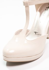 Chaussure à talon haut avec bride en T en cuir verni beige, bout rond et semelle plateforme, vue en gros plan de face et de côté.
