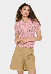 Top rosa in pizzo a maniche corte con orlo e colletto scallop, caratterizzato da un delicato motivo. Abbinato a pantaloni corti beige a vita alta.