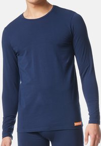 Granatowa koszula z długim rękawem, wykonana z miękkiego, elastycznego materiału. Posiada okrągły dekolt oraz małą, kontrastującą metkę marki na dole.