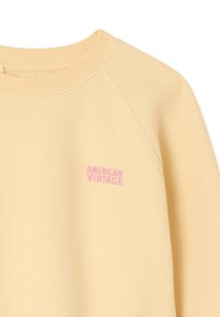 Yellow sweatshirt with ribbed neckline and raglan sleeves. Features a small pink "AMERICAN VINTAGE" logo on the front.