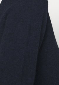 Granatowy sweter o miękkiej fakturze, z lekko luźnym krojem i wyraźnym wzorem na rękawach. Materiał wydaje się ciepły i przytulny.