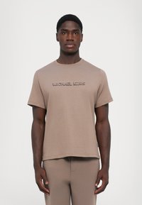 Beige bomull t-skjorte med rund hals og korte ermer, med hevet "MICHAEL KORS" bokstaver over forsiden. Enkelt design.
