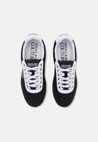 Sorte semskete sneakers med hvite skolisser og merkevare. Har en rund tå og kontrasterende detaljer på sålen og tungen.