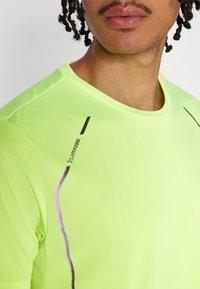 Félfényes lime zöld sport póló kerek nyakkal, fekete és lila részletekkel, valamint a "Climacool" logóval a bal felső oldalon.