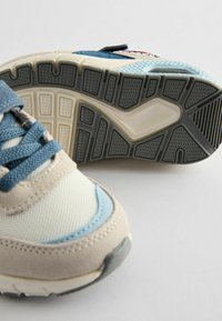 Buty sportowe z siateczkową cholewką w odcieniach beżu i jasnoniebieskiego, z teksturowaną podeszwą z czarnymi kauczukowymi akcentami i wyściełanym językiem.
