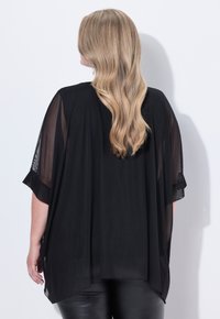 Fließender schwarzer Kimono mit durchsichtigen Ärmeln und einem längeren hinteren Saum, aus leichtem Stoff gefertigt. Glatte Textur ohne sichtbare Muster oder Akzente.