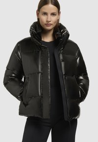 Doudoune noire à finition brillante, dotée d'un col haut, d'une texture matelassée et de boutons à l'avant. Elle a des poches latérales et une coupe décontractée.