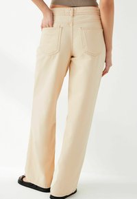 Brede, pastelbeige broek van zachte stof; heeft twee achterzakken met contrasterende stiksels en een ontspannen pasvorm.