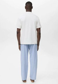 Vit t-shirt med kort ärm, kombinerad med blå och vita randiga pyjamasbyxor. Tyget ser mjukt ut; byxorna har en avslappnad passform och vertikalt mönster.