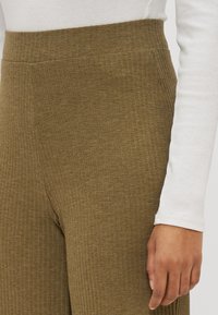 Olive green ribbed knit trousers with a high waist and side pockets, paired with a long-sleeve white top featuring a textured design.