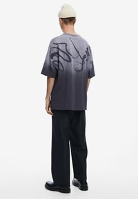 Camiseta gris de gran tamaño con un degradado de claro a oscuro, con un gráfico abstracto negro en la parte posterior; combinada con pantalones anchos negros y botas.