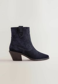 Stivali alla caviglia in camoscio blu navy con punta affusolata e tacco squadrato. Presentano un tassello laterale e dettagli di cuciture sottili sulla tomaia.