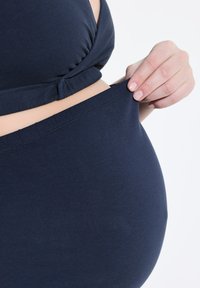 Tmavě modrý těhotenský top se sklady, kombinovaný s odpovídajícími elastickými kalhotami, které se vyznačují měkkou strukturou a elastickým pasem.