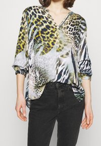 Sileä, kuvioitu paita, jossa on sekoitus eläinkuoseja vihreissä, mustissa ja harmaissa sävyissä. Löysä istuvuus, V-aukko ja käärityt hihat.