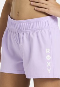 Shorts lilas en tissu léger, avec une ceinture élastique et "ROXY" imprimé en blanc sur le côté, accompagné d'un logo cœur.