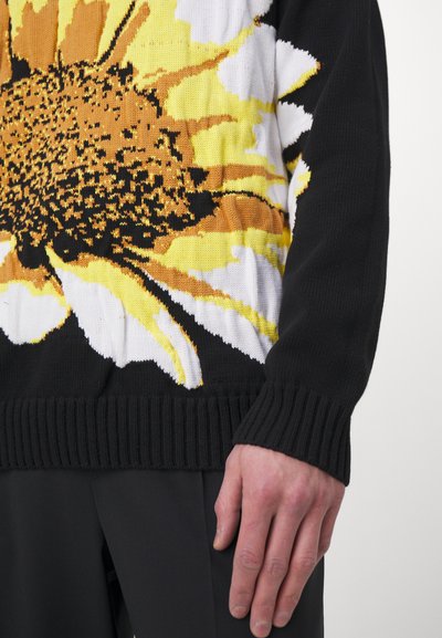 Schwarzer Strickpullover mit einem Sonnenblumenmuster in Gelb-, Braun- und Weißtönen. Gerippte Bündchen und Saum sorgen für Textur.