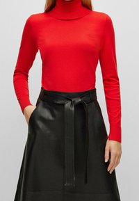 Röd långärmad polokrage topp med en smal passform. Matchad med en svart läderkjol som har ett knytbälte och sidofickor.