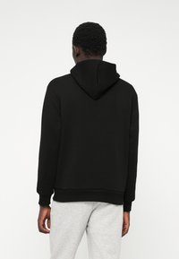 Felpa nera con finitura testurizzata, dotata di cappuccio posteriore, polsini a coste e fascia in vita, abbinata a pantaloni della tuta grigi chiari.