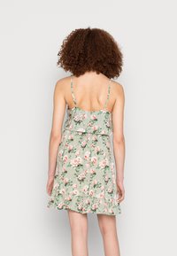 Vestido floral com alças de espaguete ajustáveis, tecido verde claro, hem rufado, padrão de flores rosa e brancas, leve, design casual.