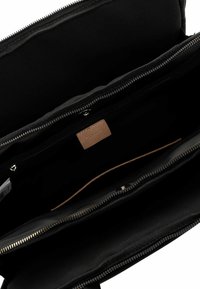 Black fabric bag interior with multiple compartments. Features zipper closures and a leather accent. Soft texture and structured design.