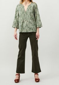 Ljusgrön mönstrad blus med V-ringning och plisseringar, matchad med mörkgröna utsvängda jeans och bruna plattformssandaler.