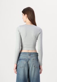 Grå langermet kort topp laget av glatt stoff. Kombinert med høy midje lyseblå denim vide benbukser med baklommer.