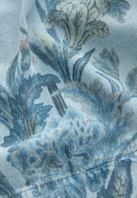 Tissu en denim bleu clair avec imprimé floral détaillé en bleu et beige et coutures visibles.