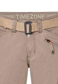 Beige katoenen broek met een geweven riem, een ritszak met een rode accent en gestikte details op de tailleband en zakken.
