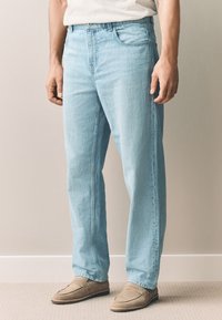 Jeans in denim azzurro chiaro con taglio dritto, caratterizzati da un design a cinque tasche e una chiusura con bottoni, abbinati a mocassini beige.