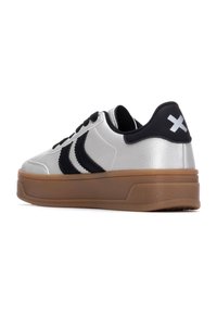 Zapatillas sintéticas plateadas con acentos negros, que cuentan con una suela gruesa de goma, superficie texturizada y dos rayas negras en cada lado.