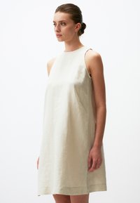 Helles beige Leinenkleid mit ärmellosem, A-Linien-Design. Verfügt über einen schlichten Ausschnitt und eine minimalistische Textur, die knapp über dem Knie endet.