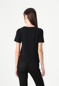 T-shirt noir à manches courtes en tissu extensible, avec un col rond et une coupe ajustée, sans motifs ni accents visibles.