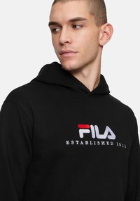 Felpa nera con cappuccio regolabile, con logo "FILA" ricamato in rosso e bianco e la scritta "ESTABLISHED 1911" sotto. Tessuto morbido.