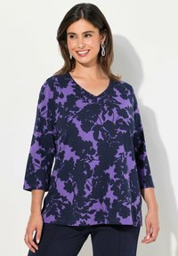 V-pääntie, kolmanneksi varttimeksi hihat ykkönen purppurassa, jossa tumma kukkakuosi. Pehmeä kangas rennolla istuvuudella ja näkyvillä ompeluseikoilla.