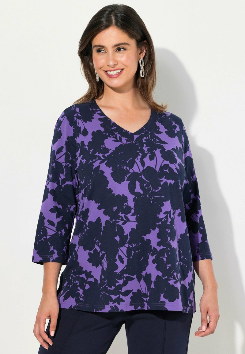 V-pääntie, kolmanneksi varttimeksi hihat ykkönen purppurassa, jossa tumma kukkakuosi. Pehmeä kangas rennolla istuvuudella ja näkyvillä ompeluseikoilla.