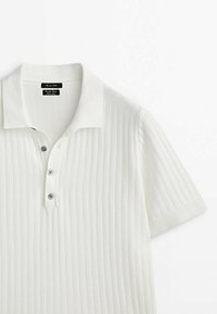 Polo en maille côtelée blanche à manches courtes avec un col et trois boutons foncés sur la patte de boutonnage.