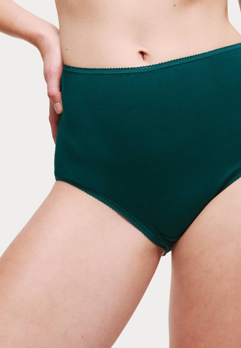 Braguita de algodón verde oscuro de tiro alto con textura suave y detalle de cintura en forma de ondas, que presenta un diseño sin costuras en las aberturas de las piernas.