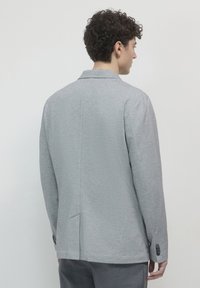 Blazer grigio con finitura liscia, design sartoriale, spacchetto singolo e tre bottoni sui polsini, visto da dietro.