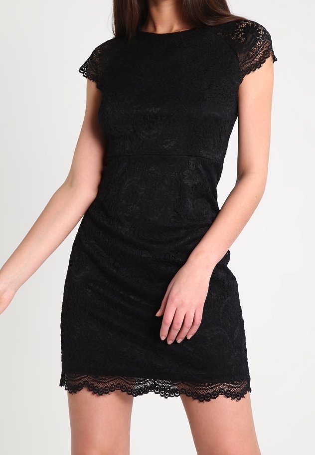 Femme portant une robe noire en dentelle à manches courtes ajustée avec un ourlet festonné, debout devant un fond clair uni.