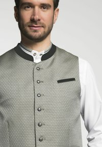 Šedá vzorovaná vesta s mandarínským límcem, pěti kovovými knoflíky a černým detailem kapsy, nošená přes bílé tričko.