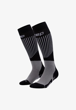 Kompressionssocken mit einem schwarzen oberen Teil, weißen vertikalen Streifen und grauen unteren Abschnitten, hergestellt aus einem strukturierten Material.