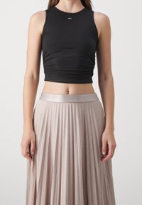 Top corto nero con dettagli arricciati sui lati, abbinato a una maxi gonna plissettata di un leggero beige con una cintura lucida.