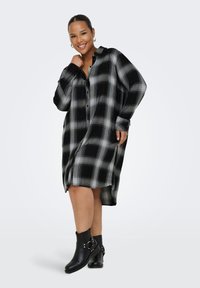 Black and white plaid shirt dress with a button-up front, long sleeves, and a relaxed fit. Worn with black ankle boots featuring hardware accents.