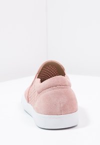 Růžové semišové slip-on tenisky s perforovanými detaily a bílou gumovou podrážkou, zobrazené ze zadní strany na bílém povrchu.